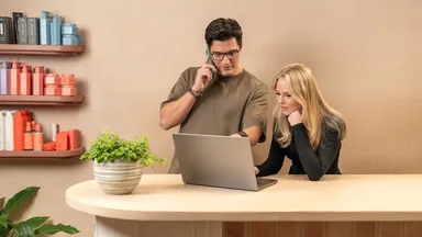 Two people using the computer at a salon's front desk.