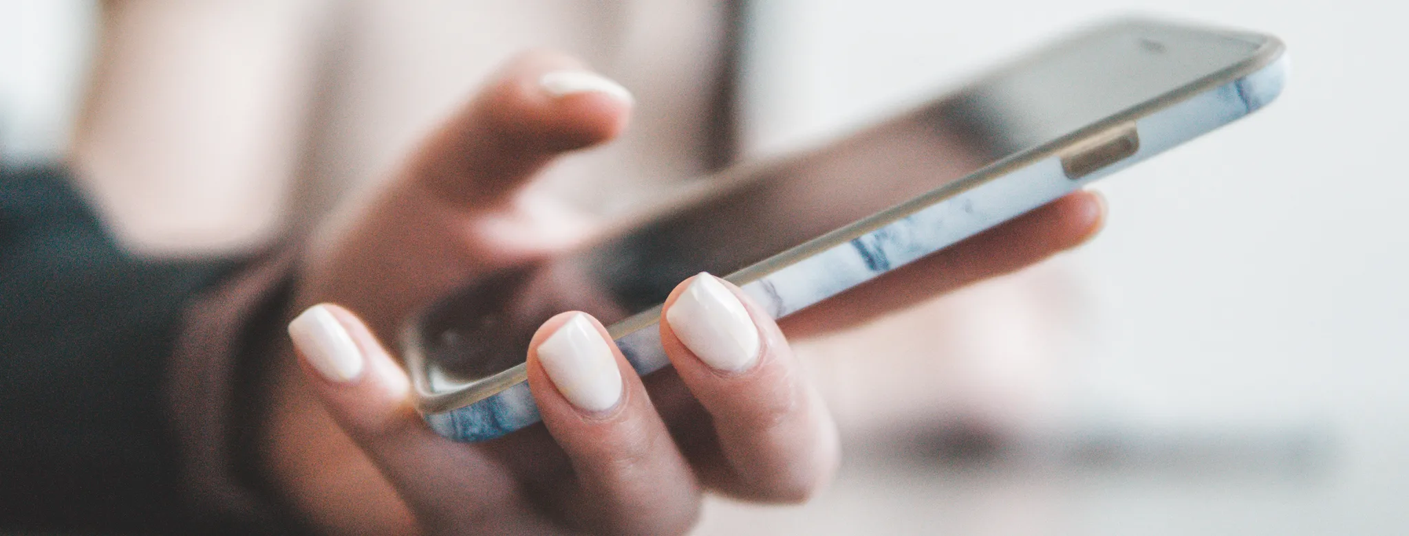 woman with light pink manicure holding smartphone