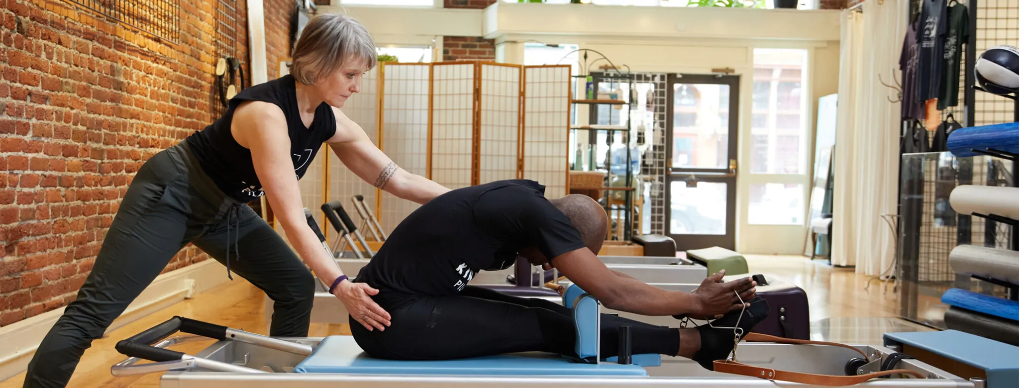woman helping man on pilates reformer machine in studio