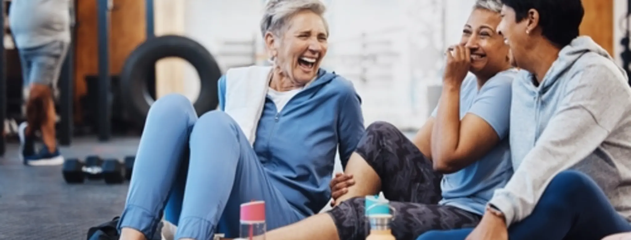 Three women in blue shirts sitting and laughing after a workout class