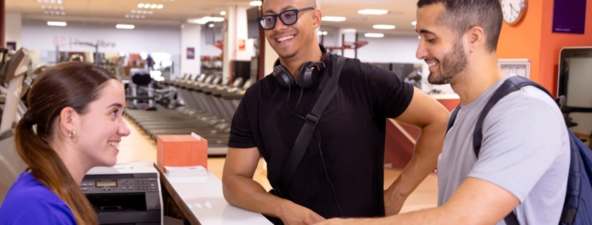Two men happily chatting with a gym receptionist as she shows them a document